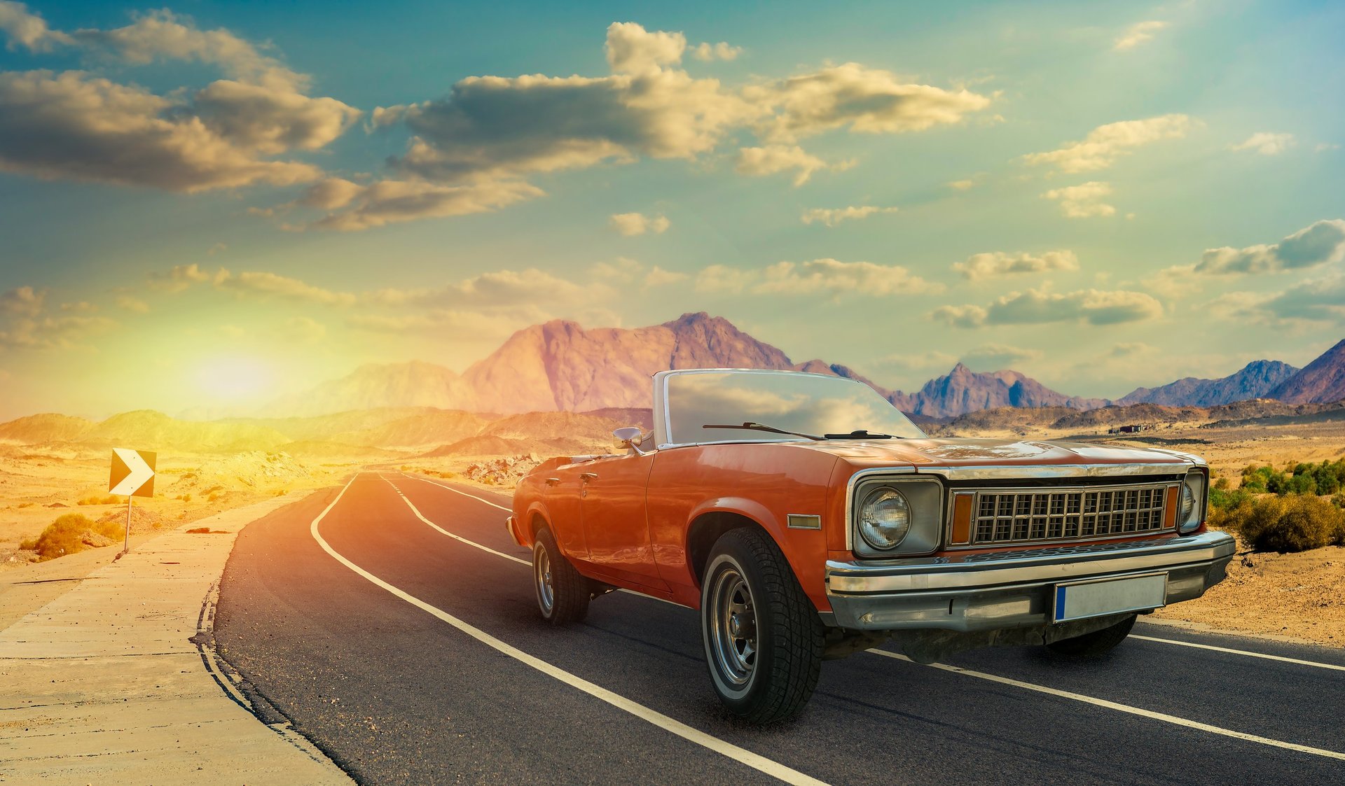Vintage red car on mountain road at sunset