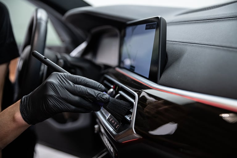 Car detailing employee carefully cleans the air vents with a brush