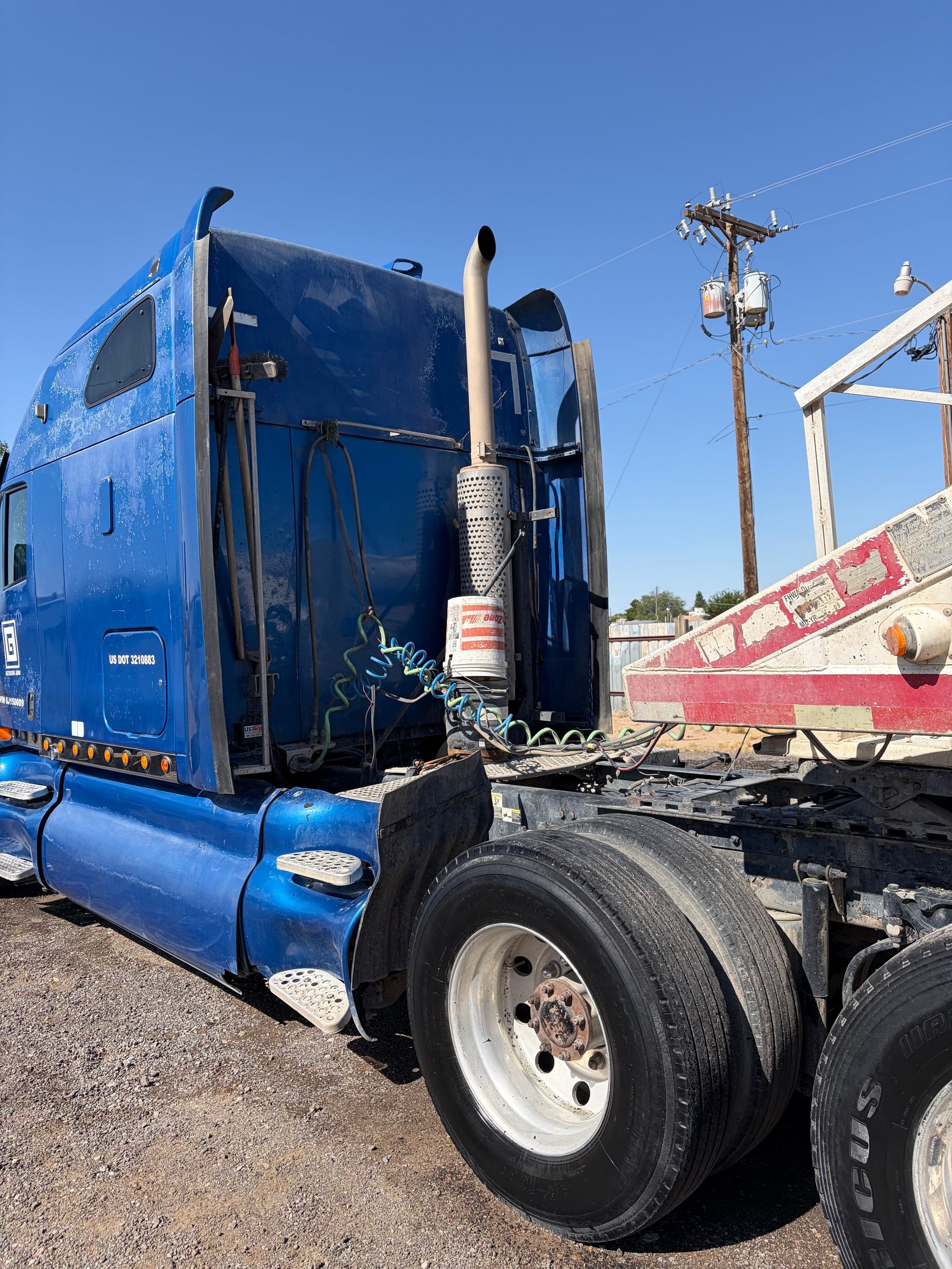 Blue semi truck cab parked at truck yard with red trailer and communications tower in background