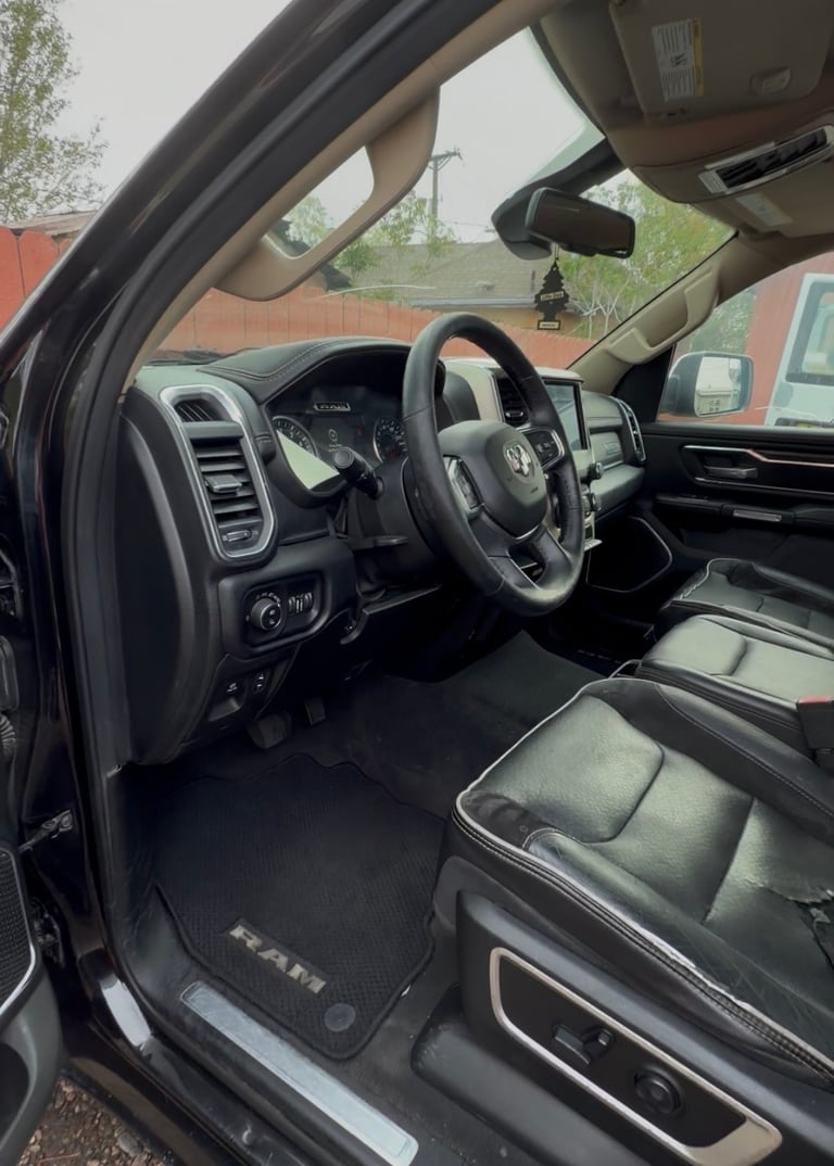 Interior view of a pickup truck showing steering wheel, dashboard, and front seats with brick building in background