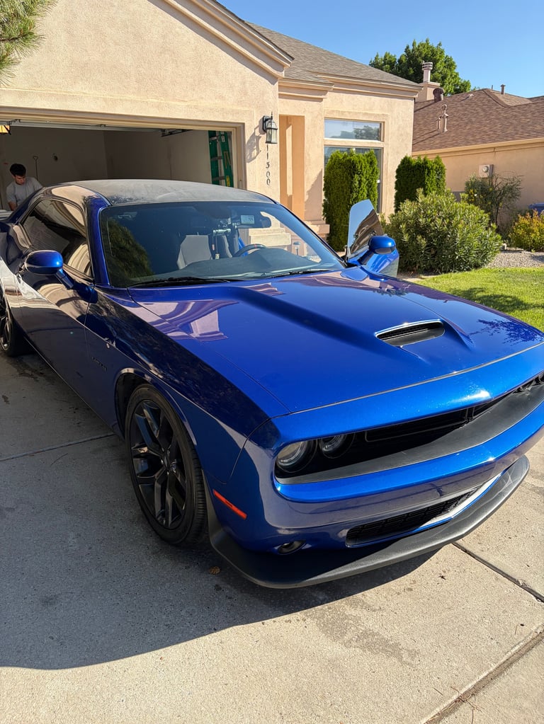 Bright blue Dodge Challenger muscle car parked in a residential driveway with garage and landscaping visible