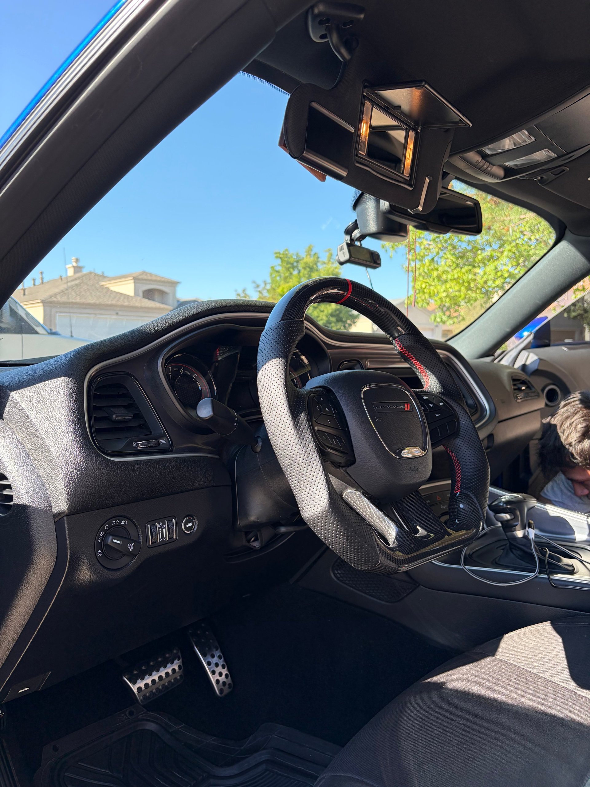 Interior view of a car from drivers seat showing steering wheel, dashboard, and windshield with residential neighborhood visible outside